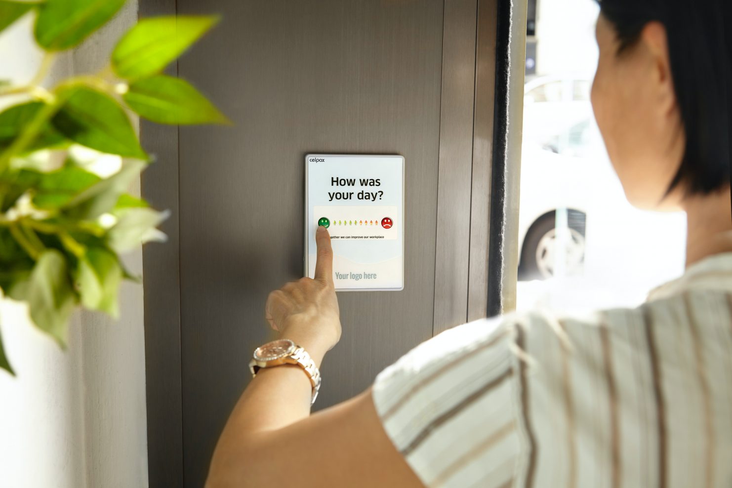 Female employee pressing a green button to give feedback on a device at the office exit door